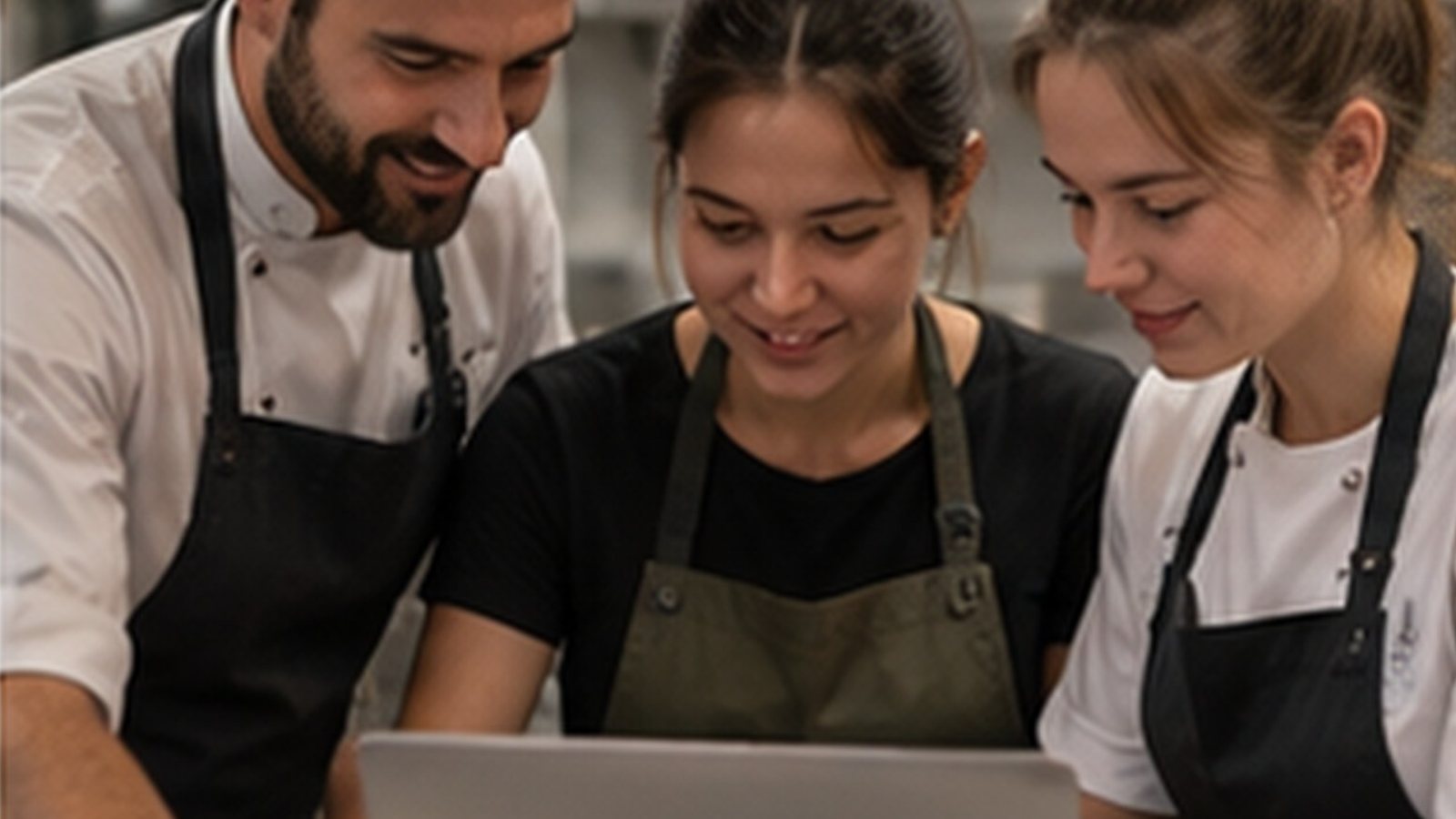 Three hospitality staff in aprons looking at training courses together on a laptop